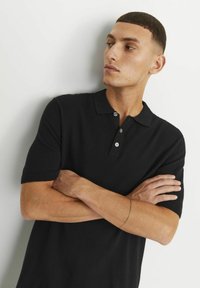 Černé pletené polo tričko s krátkými rukávy, tříknoflíkovou légou a žebrovanými manžetami. Hladká textura a přiléhavý střih.