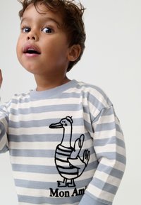 Striped long-sleeve shirt in light gray and white with a black embroidered duck graphic and text "Mon Ami" at the bottom. Cotton material.