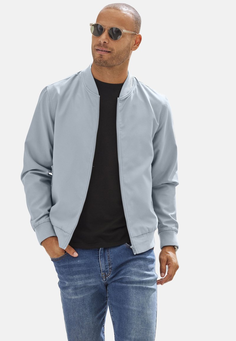 Light blue bomber jacket with a zip front, knit cuffs, and side pockets, paired with a black T-shirt and blue jeans.