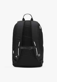 Black backpack with padded back and adjustable straps. Features a buckle closure, side pockets, and a textured logo accent.