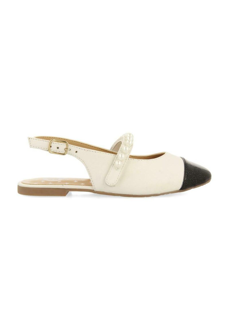 Zapato plano tipo slingback que presenta un cuerpo blanco, puntera negra, cuentas decorativas blancas en la correa y una suela marrón clara.