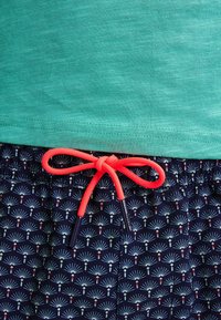 Světl zelené tričko ve spojení s námořnickými šortkami zdobenými opakujícím se vzorem bílých a červených ventilátorů. Šortky mají jasně korálovou šňůrku.