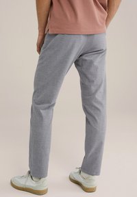 Gai pelēki austie bikses ar taisnu piegriezumu un smalku faktūru. Apvienotas ar baltām sporta apavām ar beige krāsas zoli un gaiši zaļiem akcentiem.