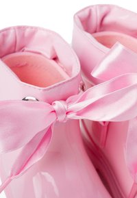 Bottes de pluie roses brillantes avec une texture lisse, des bords arrondis et des nœuds en ruban satin à l'avant. Présente des œillets métalliques pour les lacets.