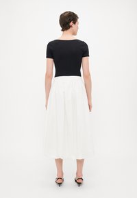 Svart kortärmad topp som är matchad med en vit, knälång, veckad kjol. Outfiten har en rund halsringning och elastisk midja.