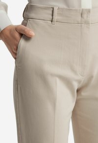 Beżowe eleganckie spodnie wykonane z gładkiego materiału, z prostym przodem, kieszeniami bocznymi oraz smukłym fasonem, z delikatnym zgięciem na przodzie.