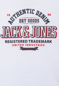 Bijela majica s crnim i crvenim grafičkim natpisom "Autentična Denim Suća Jack & Jones", s podebljanim slovima i bannerom koji kaže "Visoka Kvaliteta."