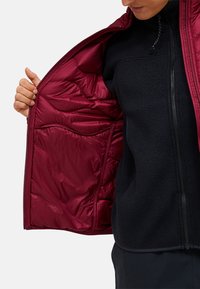 Rode pufferjack met een glanzende binnenkant en zwarte fleece voering, voorzien van een ritssluiting en een gestructureerd, gewatteerd ontwerp.