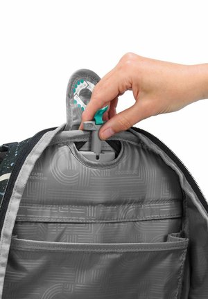 Hand adjusting gray plastic height scale inside gray backpack with zipper and internal pocket.