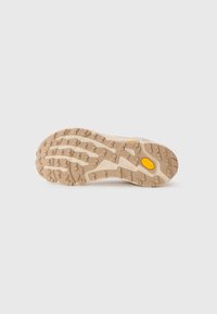 Såle av beige tursko med robust mønster og liten gul Vibram-logo nær buområdet.