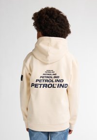 Sudadera cremosa con texto azul marino "PETROL IND" impreso en la espalda, bolsillo canguro y puños acanalados. Material suave con un corte relajado.