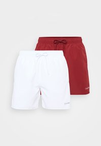 Ensemble de deux shorts de bain : un blanc, un rouge, tous deux avec une taille élastique et un cordon de serrage. Présente le logo "Calvin Klein" en blanc.