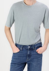 Světle šedé bavlněné tričko s krátkými rukávy a kulatým výstřihem, doplněné tmavě modrými džínami s klasickým střihem a pětipokládkovým designem.