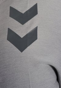 Grauer Stoff mit einer strukturierten Oberfläche, der im oberen Bereich zwei überlappende schwarze Chevron-Designs aufweist.