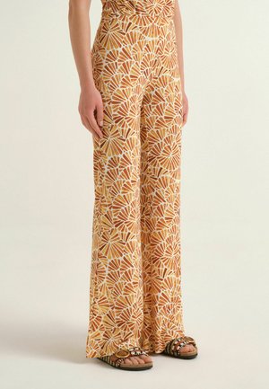 Persona che indossa pantaloni a gamba larga con motivi arancioni e bianchi tipo conchiglia e sandali aperti con cinturini decorativi.