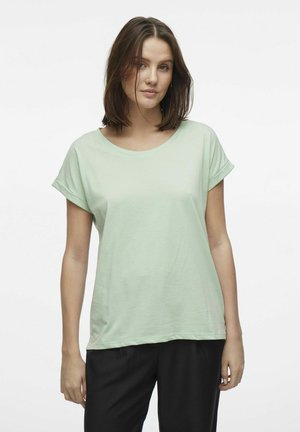 Camiseta de manga corta color verde menta con cuello redondo, textura suave, corte relajado y mangas enrolladas, combinada con pantalones negros.