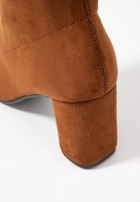 Botte à talon bloc en daim marron montrant le talon et une partie de la semelle sur fond blanc.