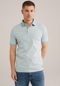 Polo cu mânecă scurtă, de culoare albastru deschis, cu un model geometric. Prezintă un guler și manșete în contrast, realizat dintr-o țesătură respirabilă.