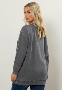 Sudadera gris de gran tamaño con mangas largas, puños y dobladillo acanalados. Textura suave. Diseño simple sin patrones o acentos visibles.