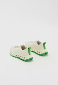 Sapatilhas brancas em malha com um superior texturizado, detalhes em verde e uma sola branca grossa com um fundo verde segmentado.