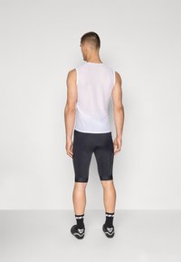 Top senza maniche bianco in rete abbinato a pantaloni ciclistici neri, con tessuto testurizzato, design aderente e dettagli a contrasto all'orlo.