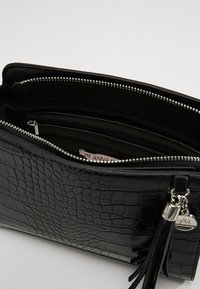 Sort krokodilleder clutch med sølv lynlås, der har et indre rum og flere lommer til organisering.