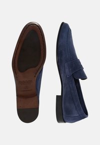 Jūras spēku zilo zamšādas mocasīnu ar plakanu zoli, noapaļotu purngalu un dekoratīvu jostu. Iekšpusē gluda ādas zolīte un dūriens akcentējošām detaļām.