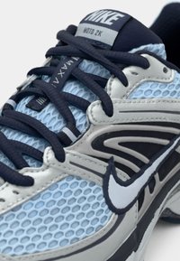 Tenisky Nike Air Max Moto 2K v svetlo modrej a šedej farbe, s priedušným materiálom, námorníckymi šnúrkami a bielym logom „swoosh“. Štruktúrované detaily na stranách.
