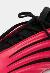 Primo piano di una sneaker nera con vivaci dettagli rossi che mostra una precisa allacciatura e un design lucido sul pannello laterale.