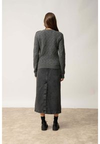 Szary sweter w splot kablowy z okrągłym dekoltem, połączony z ciemnoniebieską maxi spódnicą z rozcięciem z przodu, noszony z grubymi czarnymi butami.