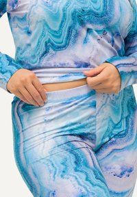 Completo activewear blu con motivo, composto da maniche lunghe e leggings a vita alta; tessuto morbido e elastico con una texture marmorizzata.