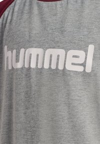Szara koszulka z krótkim rękawem z burgundowymi akcentami i dużym białym logo "hummel" na klatce piersiowej, wykonana z miękkiej, mieszanej tkaniny.