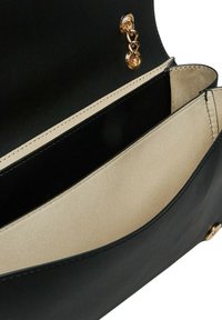 Interno della borsa in pelle nera con una fodera beige, dotata di un fermo in metallo dorato e una superficie liscia, che presenta due compartimenti.