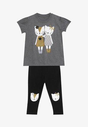 Zweiteiliges Outfit mit einem grauen T-Shirt, das eine Grafik von zwei Katzencharakteren zeigt, und schwarzen Leggings mit Katzenkopf-Akzenten auf den Knien.