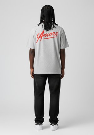 Grijze katoenen T-shirt met korte mouwen, met op de achterkant opvallende rode "Amore" tekst. Gepaarde met zwarte broeken en witte sneakers.