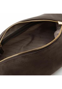 Interieur van een bruine suède tas met een gladde textuur, voorzien van een gouden ritssluiting en een voering met een lichtkleurig patroon met subtiele golfmotieven.