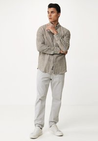 Camisa a rayas en beige y blanco, combinada con pantalones gris claro y zapatillas blancas, mostrando un ajuste casual y moderno.