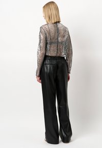 Kort metallic mesh jack met lange mouwen, gecombineerd met zwarte high-waisted leren broeken met een soepele textuur en elastische taille.