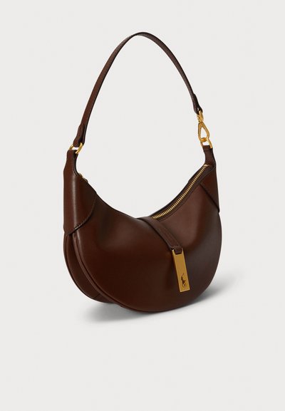 Καφέ δερμάτινη τσάντα ώμου με καμπυλωτό σχέδιο, διακοσμητικό φερμουάρ σε χρυσό χρώμα και χρυσή μεταλλική πλακέτα. Διαθέτει έναν ιμάντα για εύκολο κράτημα.