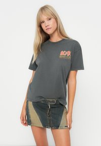Szary t-shirt z grafiką przedstawiającą "AC/DC Highway to Hell", zestawiony z dżinsową spódnicą z kontrastowymi panelami i zamkiem błyskawicznym z przodu.