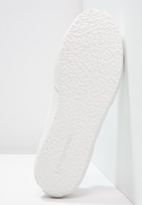 Vit sneakersula med texturerad gummi, rundad form och logotypavtryck. Släta kanter förbättrar den övergripande minimalistiska designen.