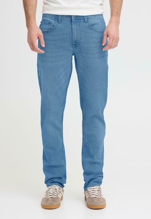 Hellblaue Jeans aus Denim mit klassischem Fünf-Taschen-Design und geradem Schnitt. Kombiniert mit grauen und beigen Turnschuhen.