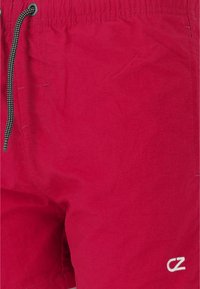 Röda badshorts i lättviktsmaterial, med en elastisk midja och en svart och vit dragsko, samt en vit logotypaccent.