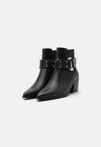 Sorte lær ankle boots med spidse tåer, en kraftig hæl og en dekorativ rem med øjet og spænde.