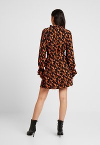 Svart klänning med orange blommönster, långa ärmar, volangärmar och en figursydd midja. Buren med svarta snörboots.