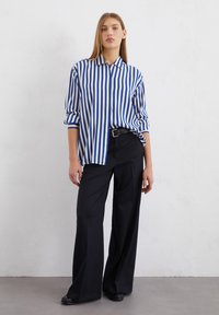 Chemise rayée bleue et blanche à manches longues, associée à un pantalon large noir. La chemise comporte un col et a une coupe décontractée.
