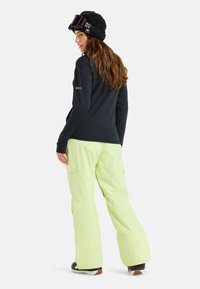 Zwarte langarmsgem shirt met "ROXY" logo, gecombineerd met lichtgroene sneeuwbroek met cargozakken, gedragen met een zwarte gebreide muts en skibril.