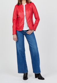 Červená kožená bunda s rovného střihu, se zipovými kapsami a kulatým výstřihem. Spárovaná s volnými modrými džíny a černými kotníkovými botami.