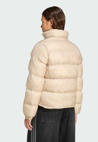 Beige puffer jacket with quilted sections, high collar, and elastic cuffs, paired with grey wide-leg pants. Smooth fabric texture.