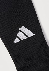 Sort atletisk sokk med teksturert strikkedesign og en tydelig hvit tre-stripe-logo. Glatt stoff, middels lengde.